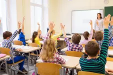 Foto av barn i klassrum som räcker upp händerna.